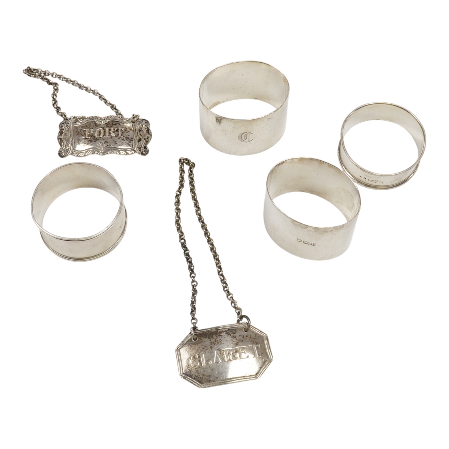 Four silver napkin rings including a pair, Sheffield, 1919, together with two George III silver wine labels, Claret, maker probably Abstinando King and Port, maker James Phipps I.